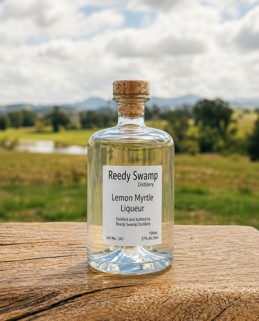 Bottle of Reedy Swamp Distillery Lemon Myrtle Liqueur on a wooden surface with a scenic Bega Valley background