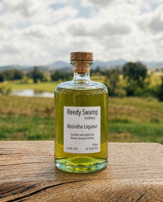 Bottle of Reedy Swamp Distillery Absinthe Liqueur on a wooden surface with a scenic Bega Valley background